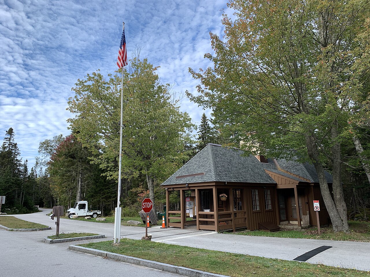 The small wooden entrance station at Seawall Campground in Acadia, with a flagpole, a stop sign and a paved entry lane
