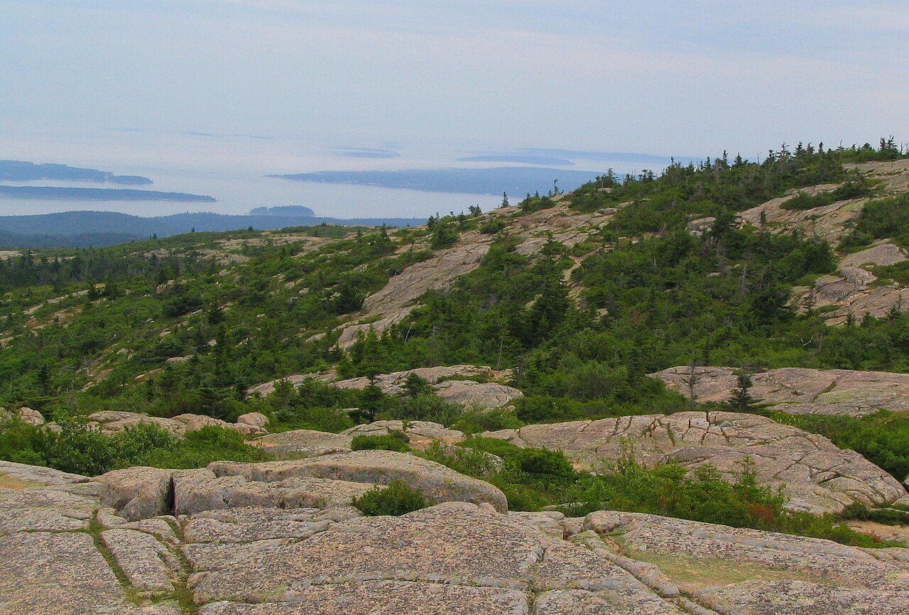 Pink granite ledges and low spruce on the slopes of Cadillac Mountain, with islands and Frenchman Bay in the haze beyond