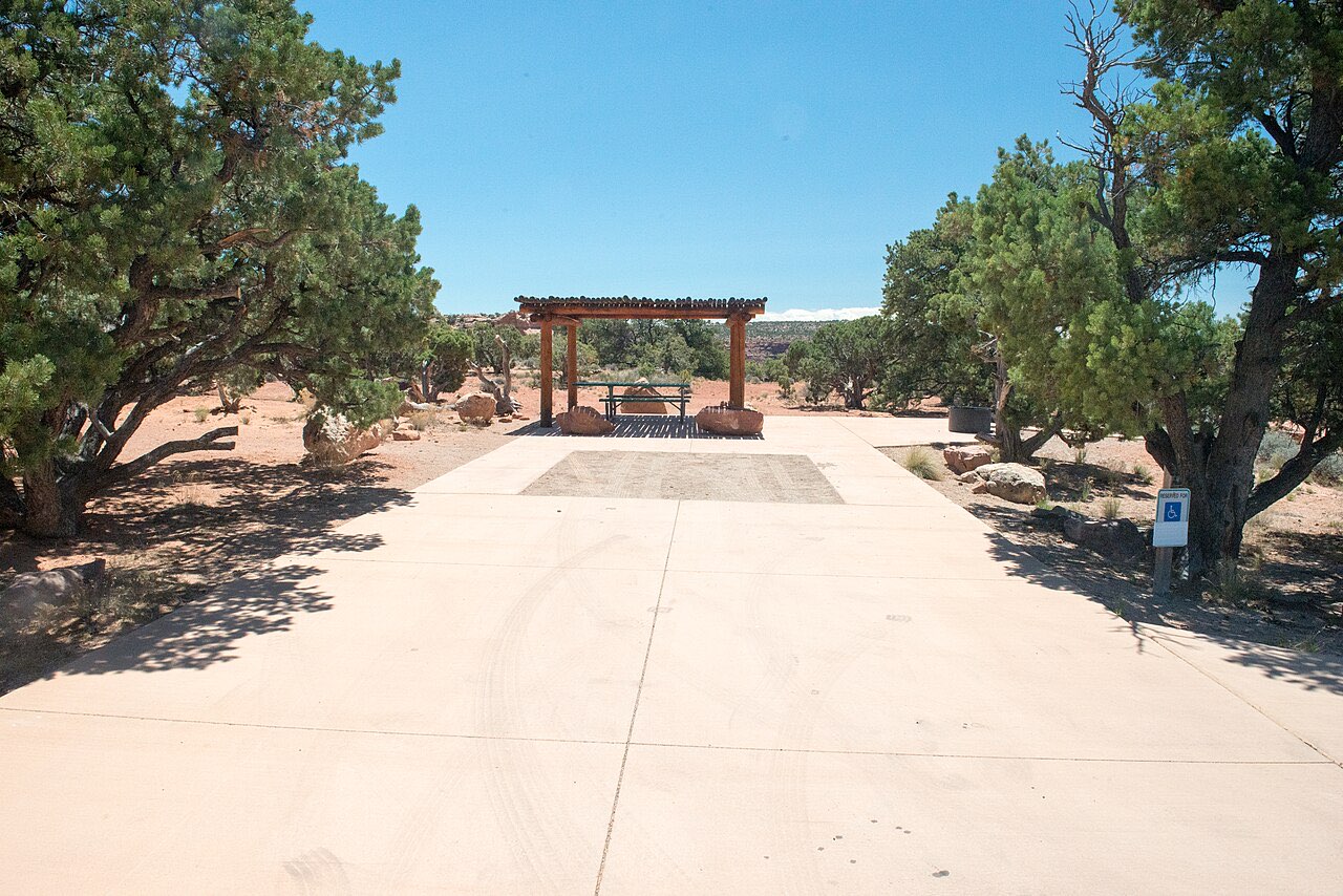 A wide concrete campsite pad with a shade shelter and picnic table at the Island in the Sky campground in Canyonlands