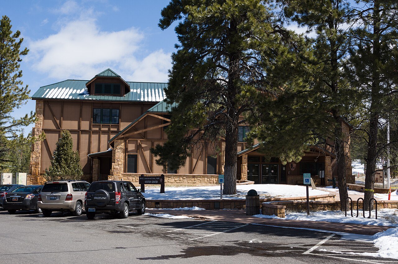 The stone and timber Bryce Canyon Visitor Center with cars in its parking lot and patches of snow on the ground