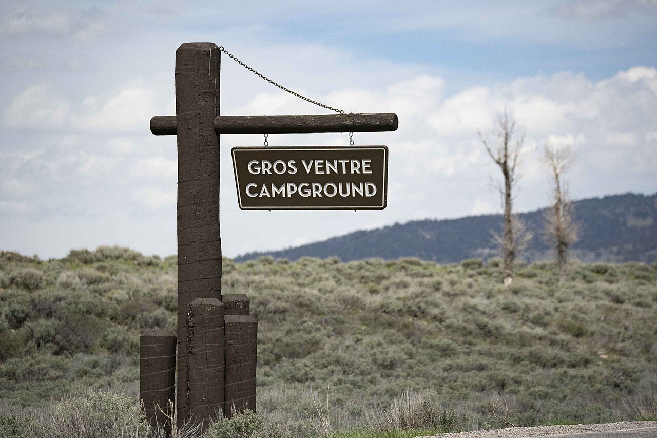 Wooden Gros Ventre Campground entrance sign hanging from a log post above sagebrush flats