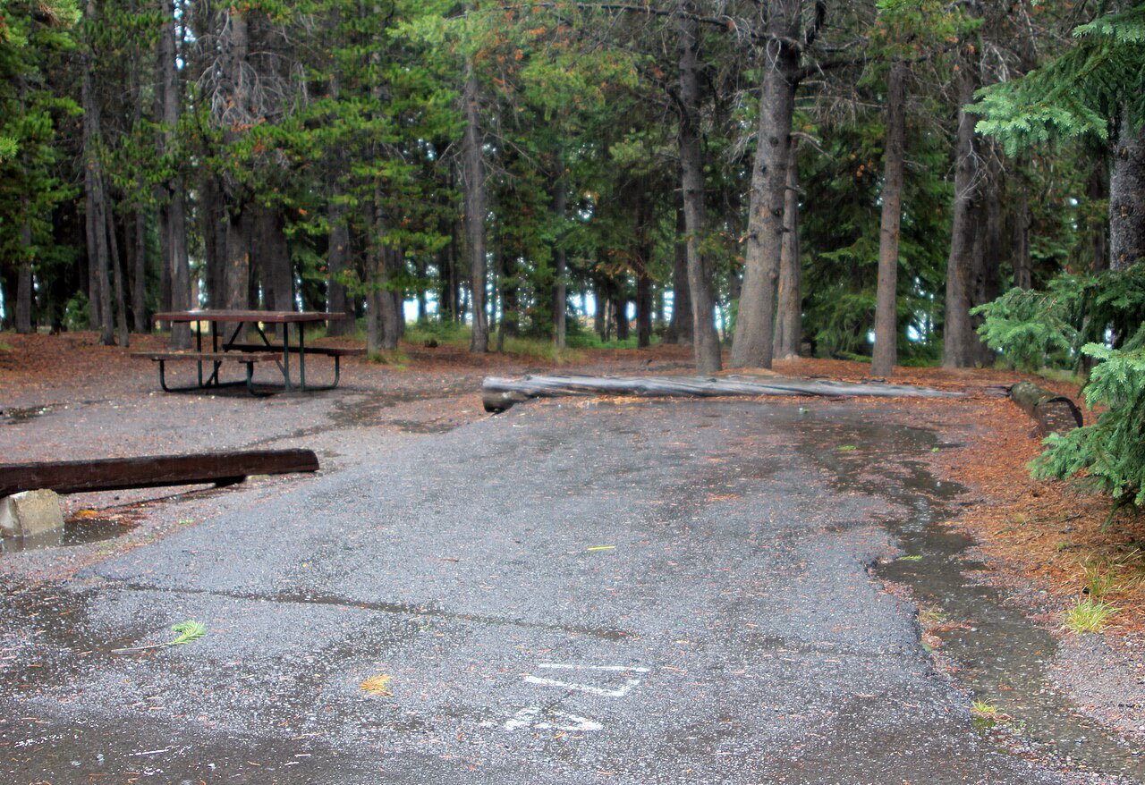 Travel trailer with its slide-out extended, leveled on wood blocks at a paved Grant Village campsite