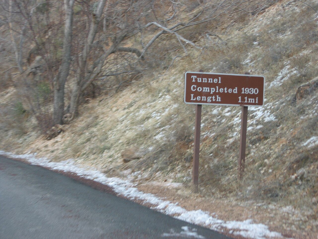 Brown roadside sign reading Tunnel Completed 1930 Length 1.1 mi on a hillside beside the Zion-Mount Carmel Highway