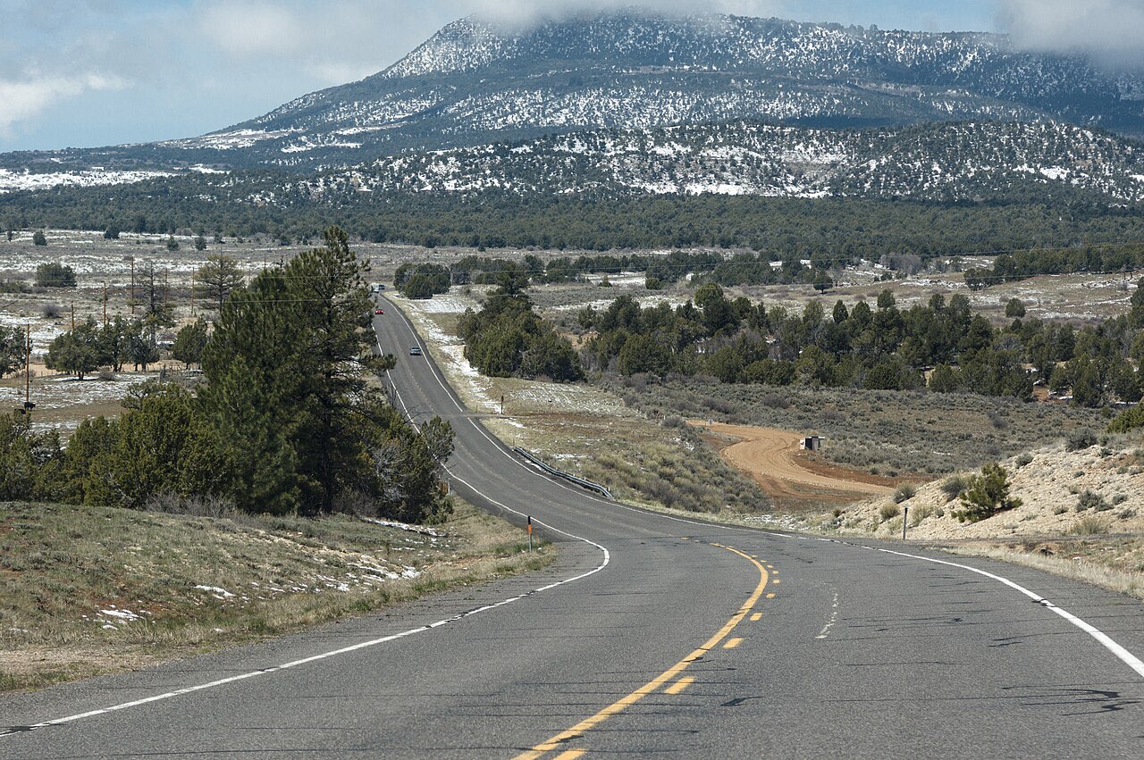 Two-lane Utah State Route 9 curving across open high-desert country toward a snow-dusted mountain